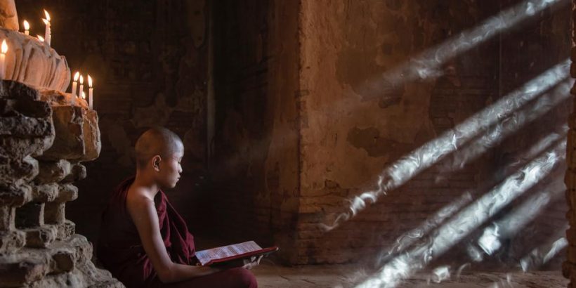 Image posé d'un moine dans une pagode entrain de lire un livre avec des ambiences de fumée et rayon de lumière.